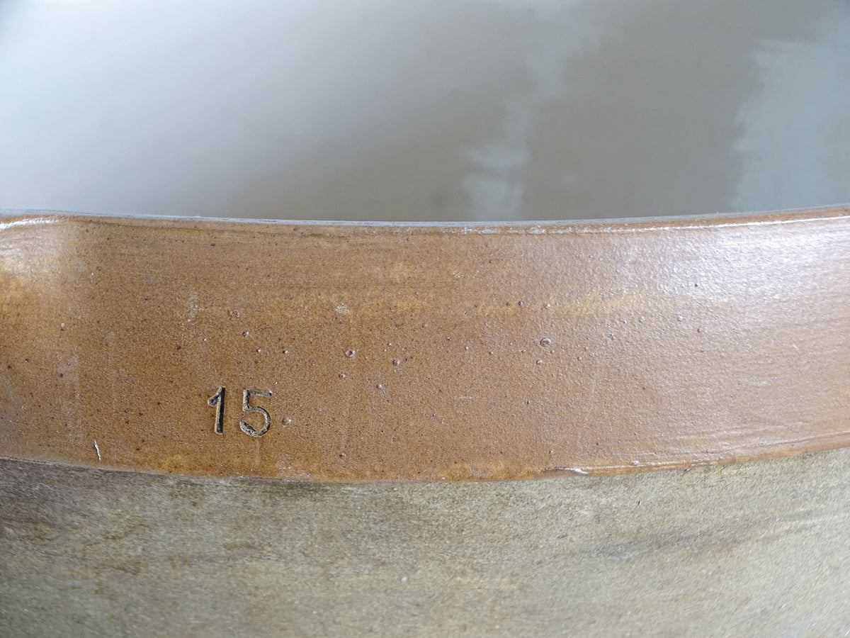 Close-up of the number 15 impressed into the warm brown glazed rim of an antique French pottery bowl.