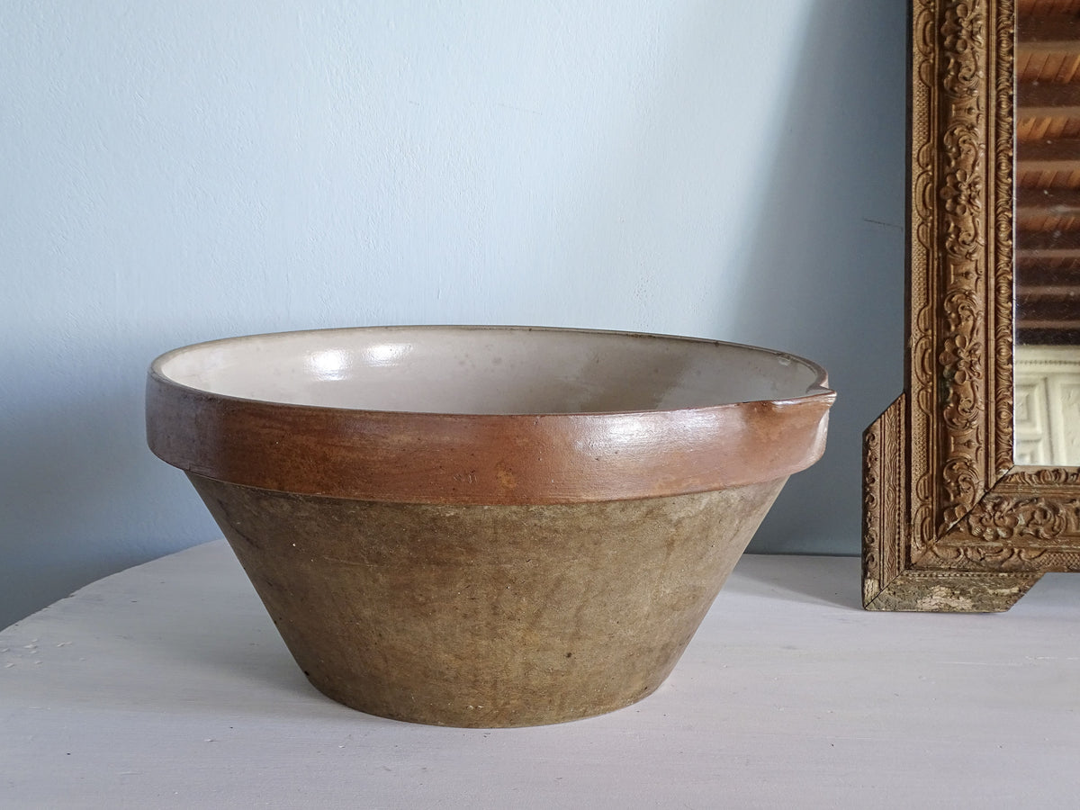 Side view of a large French antique pottery mixing bowl with sloping sides, brown glazed rim and cream interior.