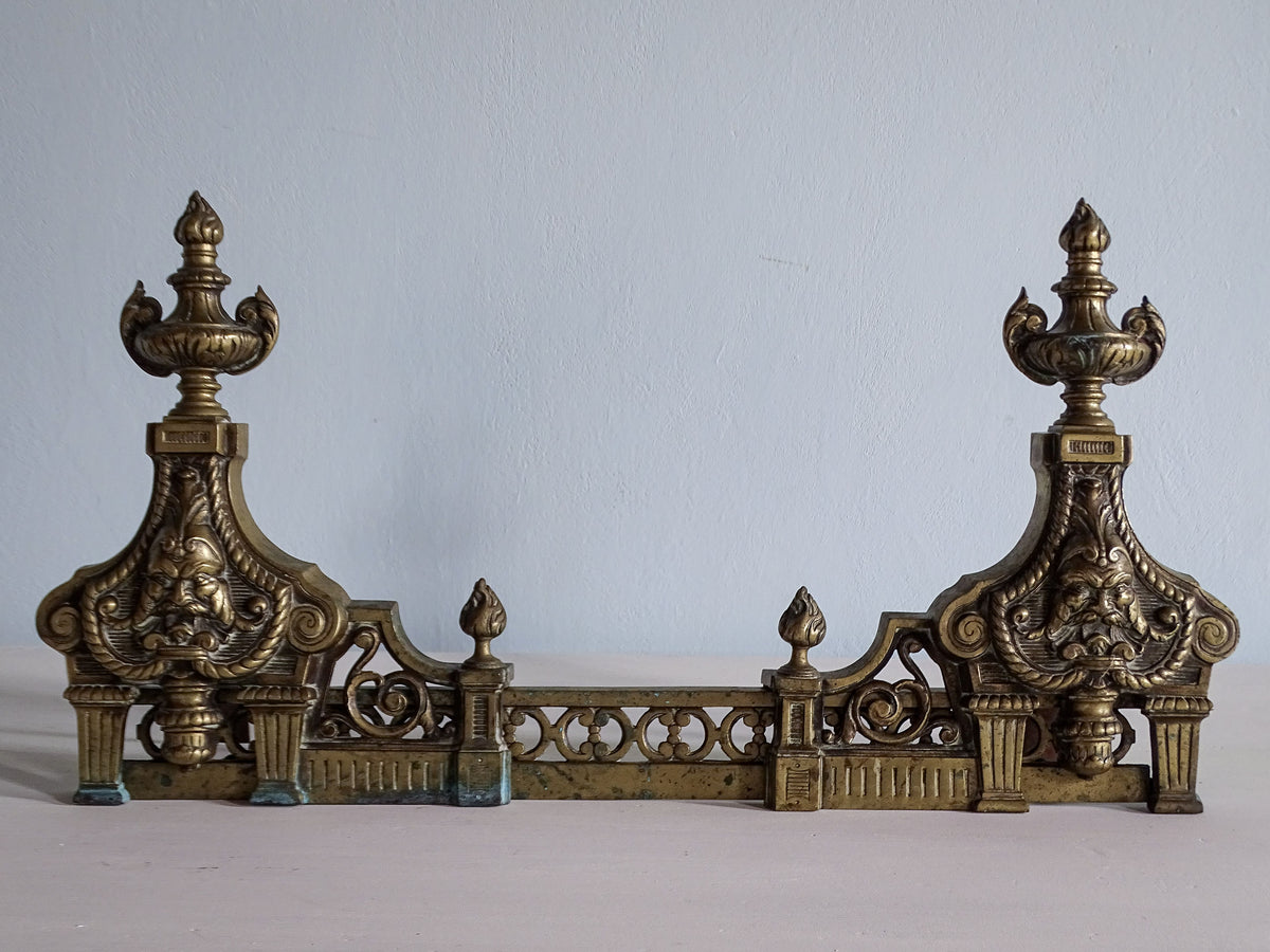 Front view of 19th-century French brass fireplace fender with ornate bearded masks, urn finials and pierced scrollwork