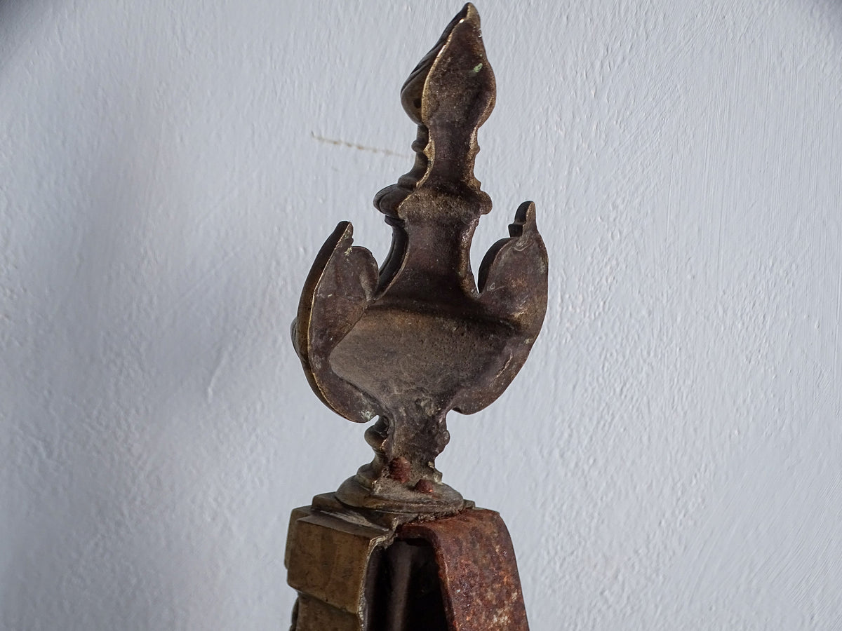 Rear view of decorative brass urn and flame finial showing aged metal and iron support