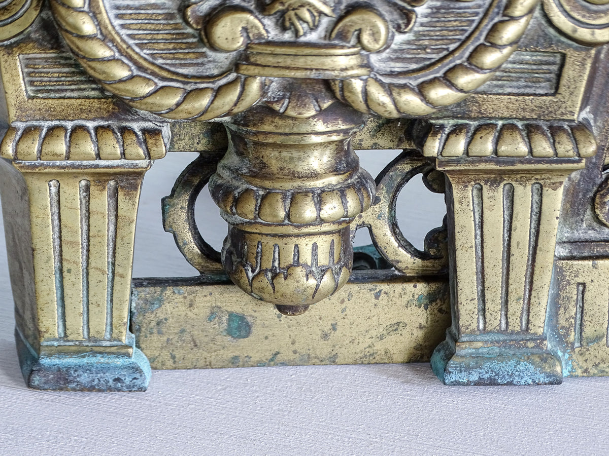 Close-up of antique brass chenet base with fluted columns, hanging ornament and areas of green verdigris