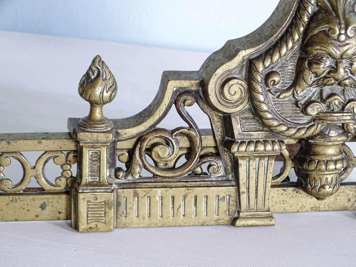 Ornate scrollwork and flame finial on the opposite side of a 19th-century French brass fireplace fender
