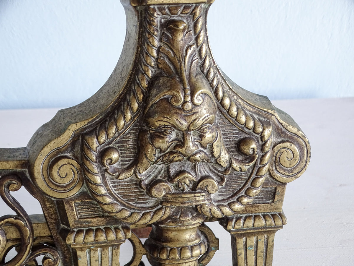 Detailed bearded mascaron surrounded by rope borders and scrollwork on an antique brass chenet