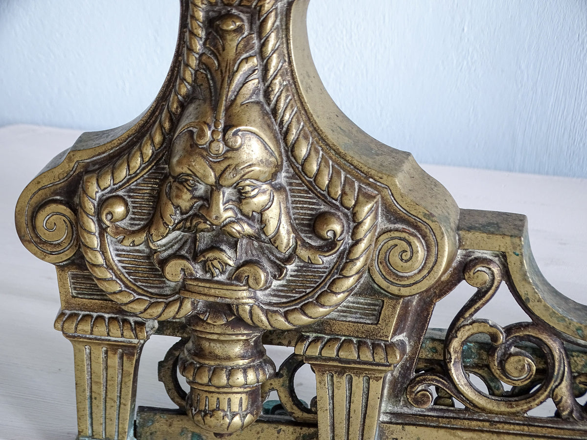 Close-up of the second ornate bearded mask with scrolling foliage and fluted columns on French brass fireplace fender