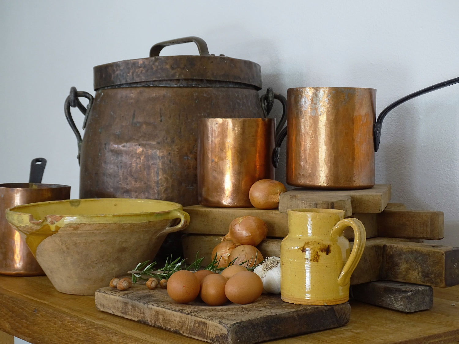 Antique French farmhouse decor: terracotta bowls, glazed pottery jugs, copper cauldron and pans, French wooden cutting boards. 