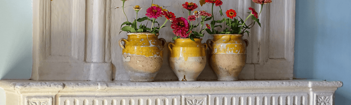 French antique confit pots filled with flowers on a country house fireplace in a room with a pale blue wall