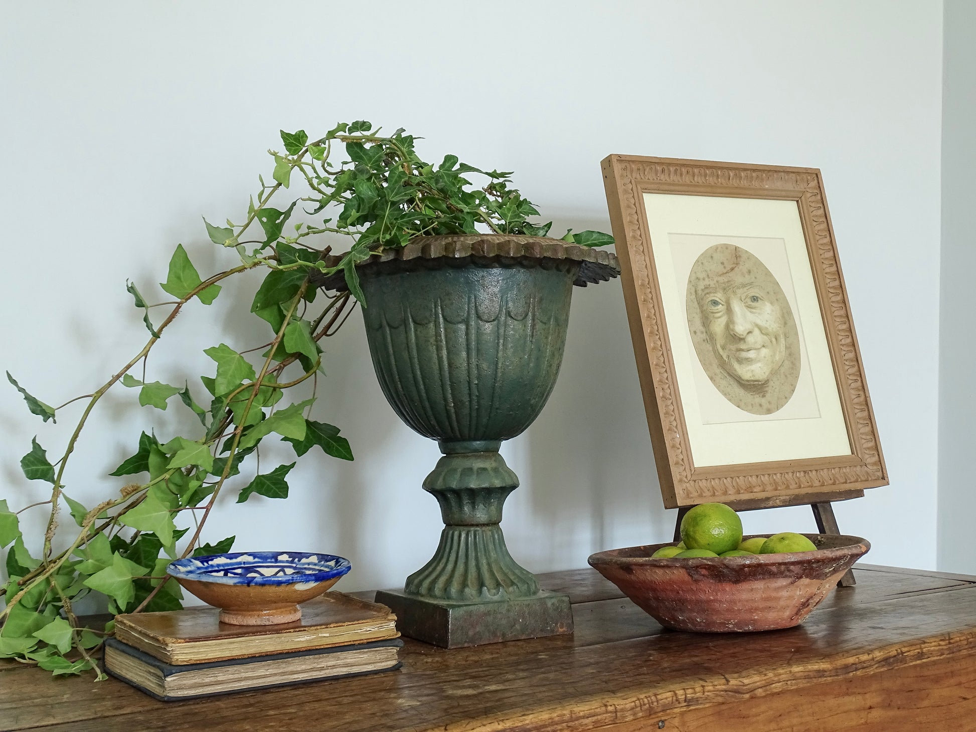 French antique cast iron urn with antique artwork and ceramic bowls on a sideboard in a French country home