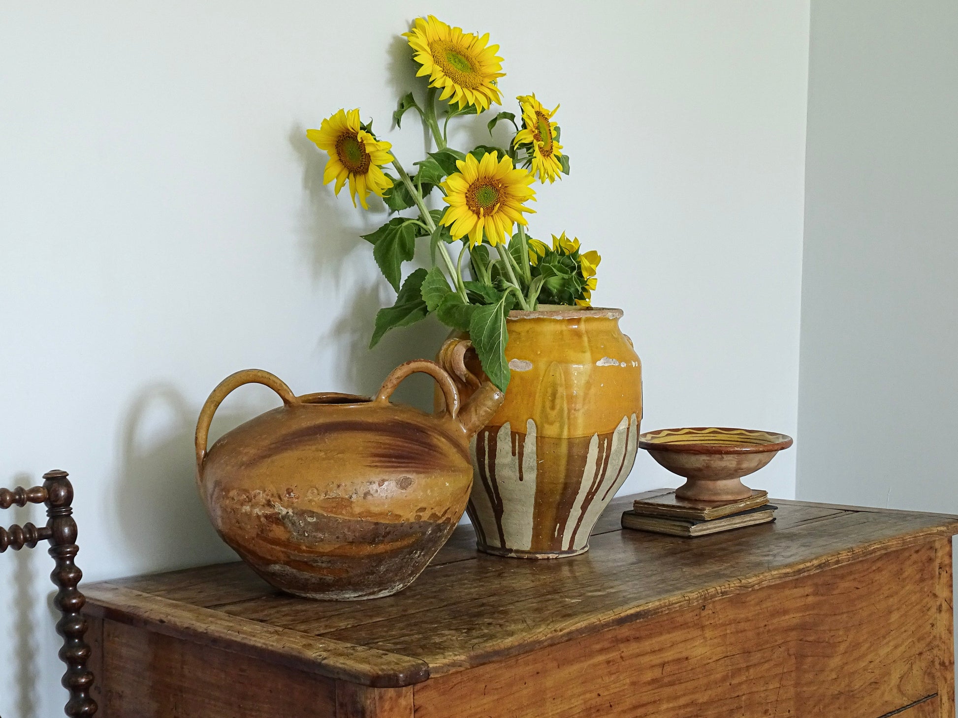 French antique ceramic jug with yellow glaze and French confit pot with sunflowers on a sideboard in a pale blue painted room in a French country interior. 