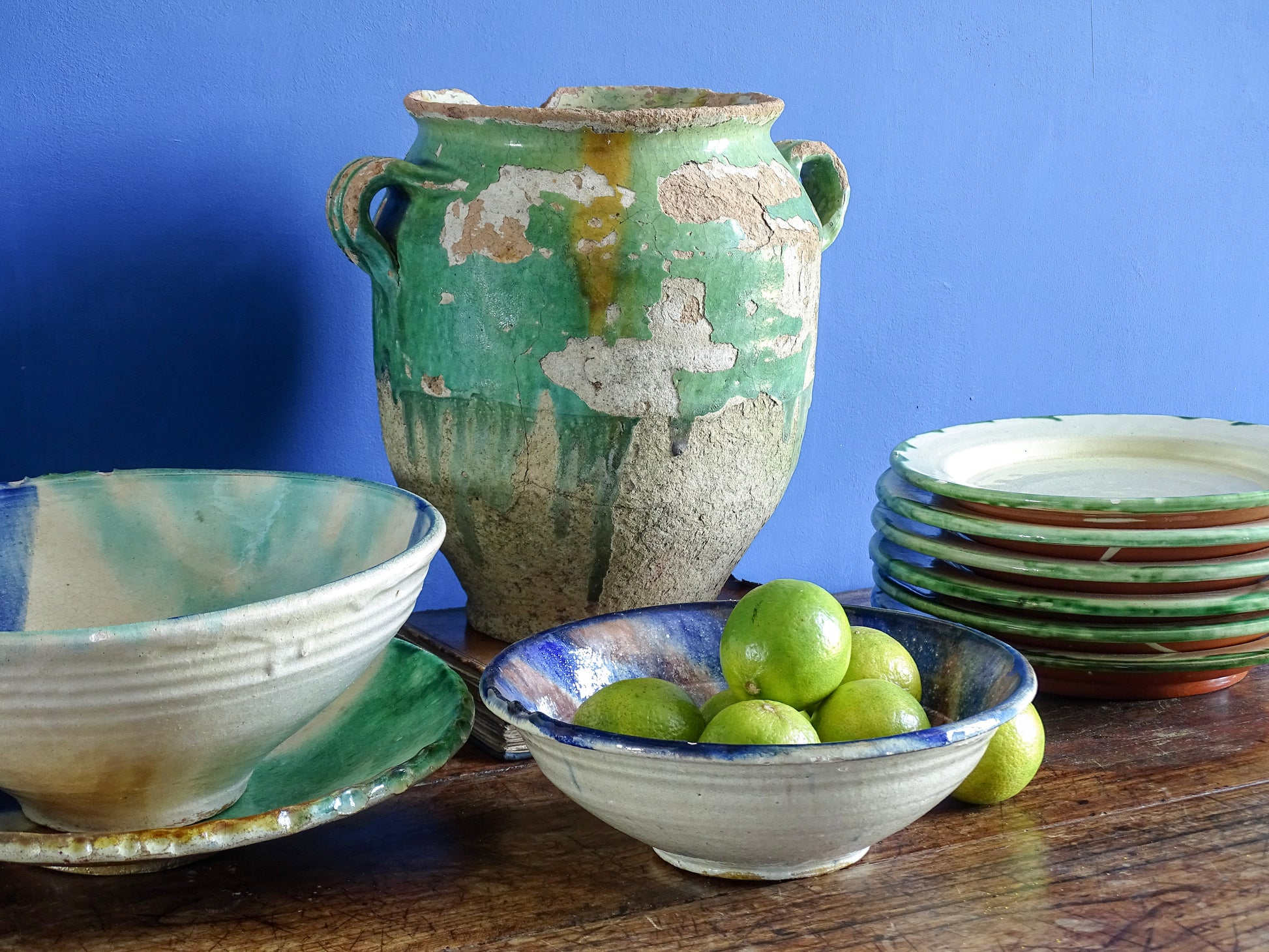 French antique confit pot with green glaze alongside ceramic bowls with blue glaze in a room with painted blue walls