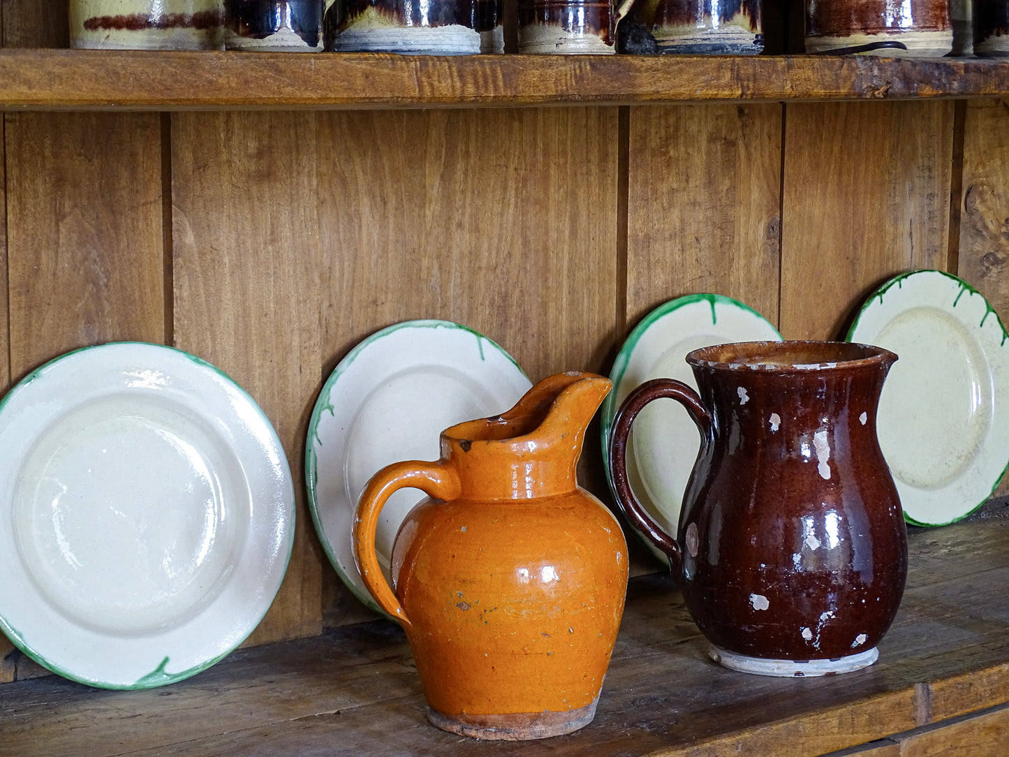 Rustic French antique pottery pitchers with ceramic plates on wooden shelves in a French country interior