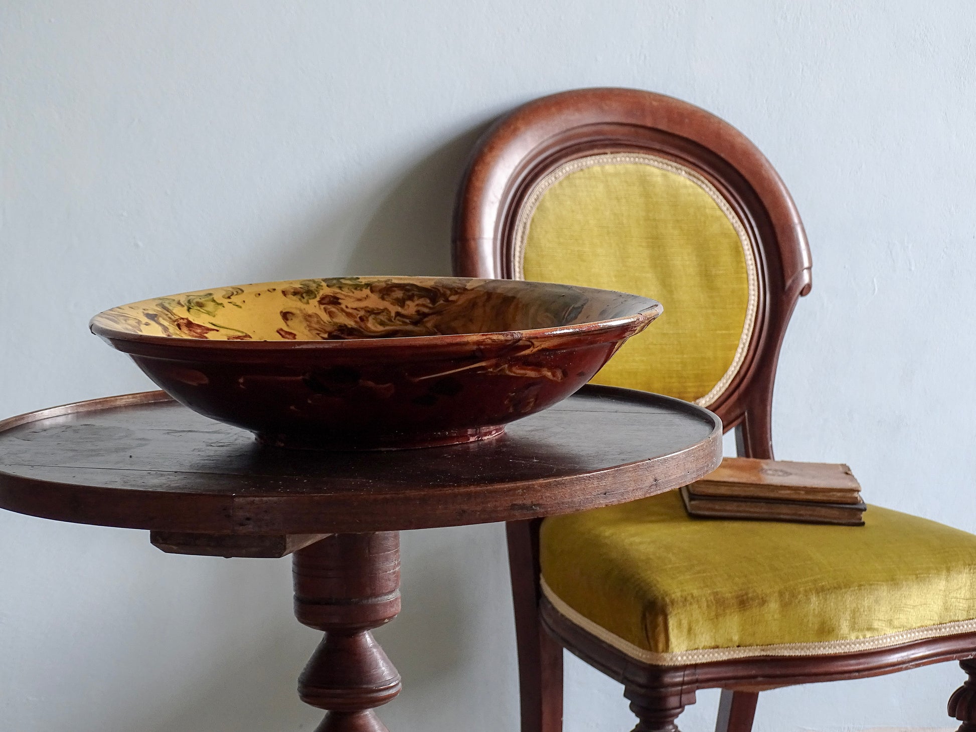 French vintage ceramic bowl with a yellow marble glaze, sitting on a table with a yellow velvet covered chair in a French country home. 