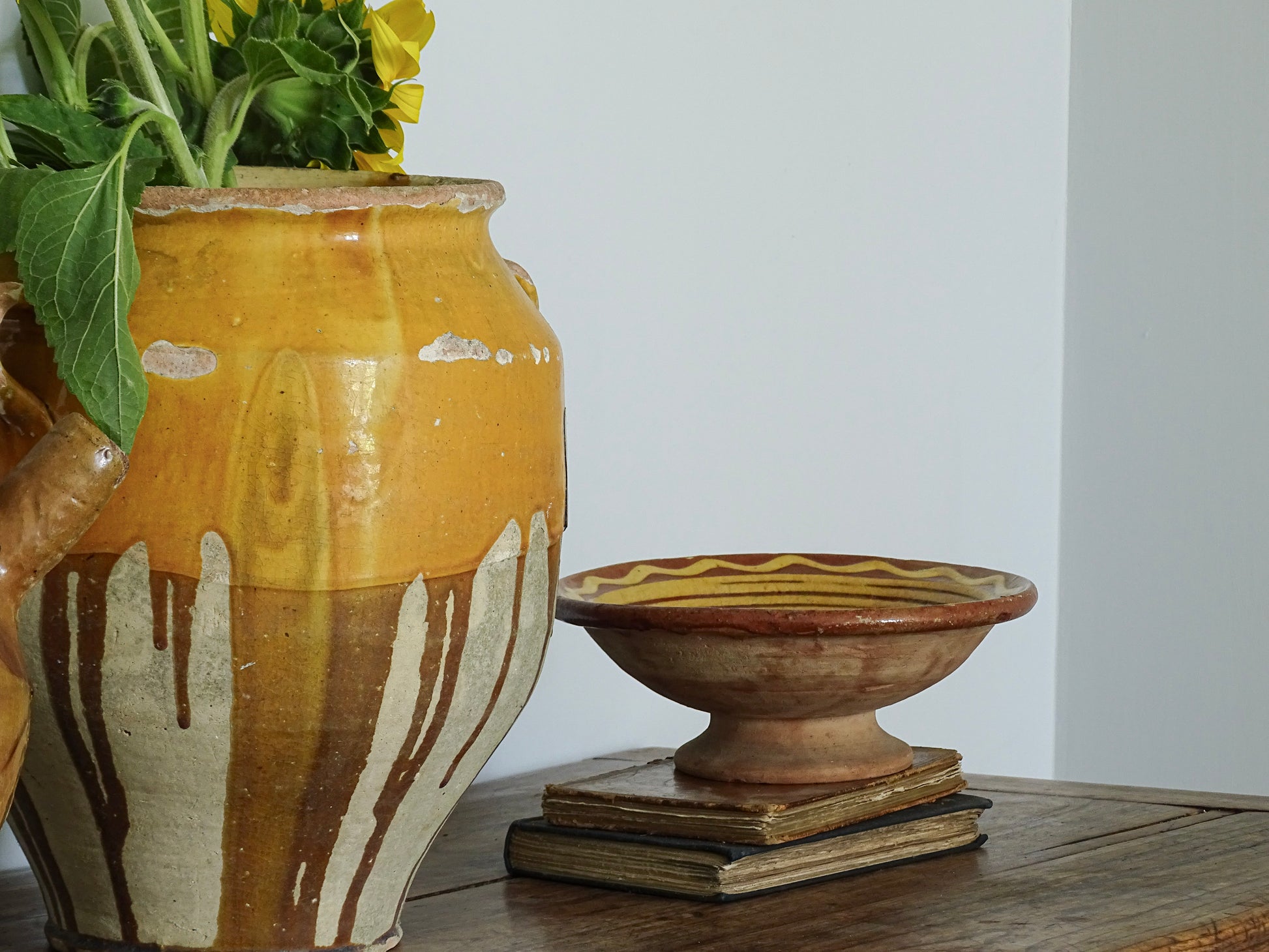 French vintage earthenware bowl with pedestal base next to a yellow confit pot on a sideboard in a blue painted room in a French country house. 